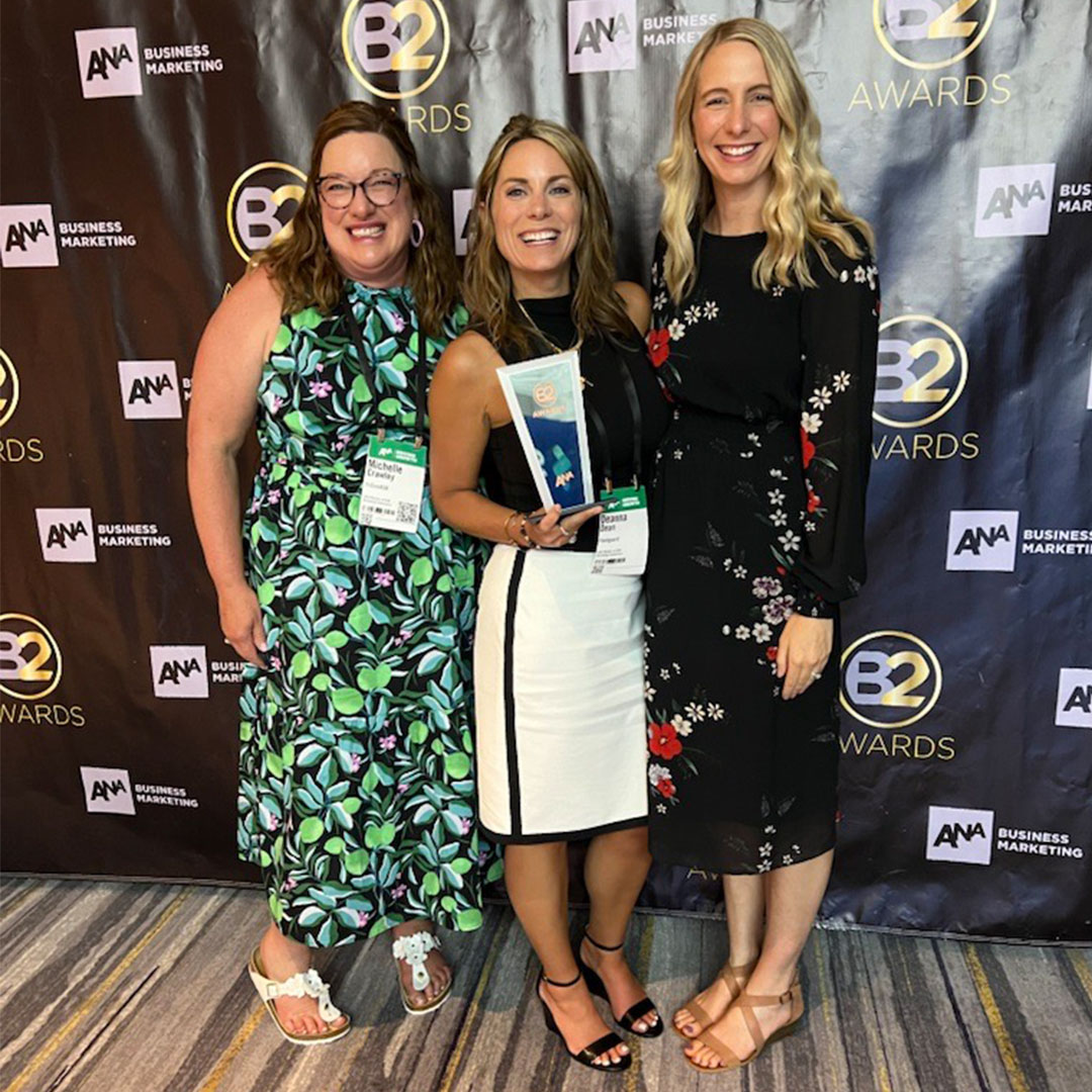 Michelle Crawley, Deanna Dean and Whitney Alexander holding the ANA B2 trophy in front of a backdrop.