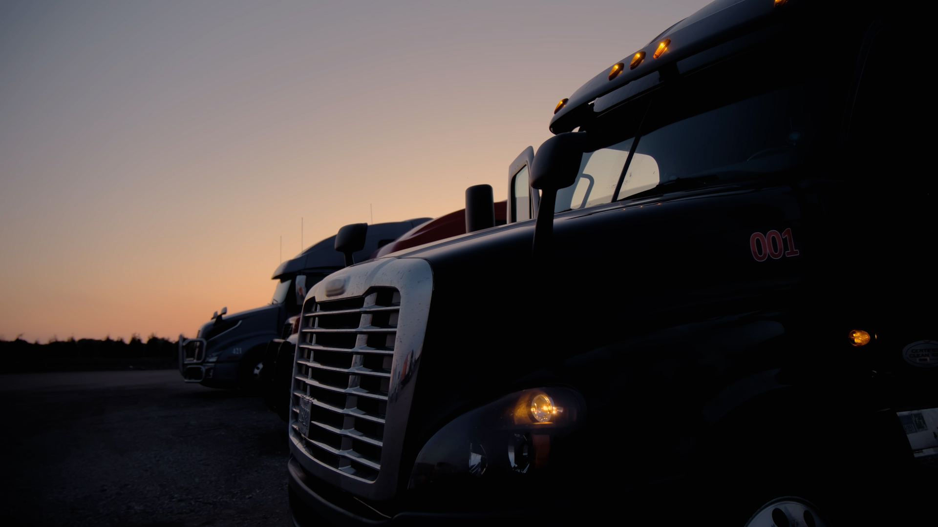 Several semi-trucks parked in the view of a sunset